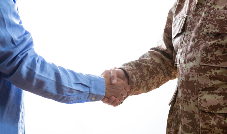Military person and civilian shaking hands standing on white background